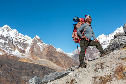Mature high Altitude Himalaya Nepalese Mountain Guide staying on rocky Slope with Backpack Climbing Gear and looking Up