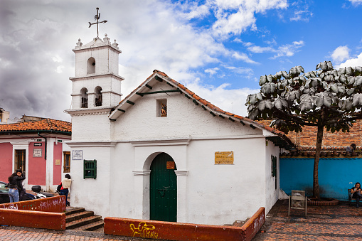 Bogota, Colombia - July 20, 2016: The Ermita or Hermitage of San Miguel del Principe on the Chorro de Quevedo in the South American, Andean capital city of Bogota, in  Colombia. The chapel was built in 1969 based on images of the Capilla del Humilladero which is SAid to have been the first chapel in the New Kingdom of Granada in the early 16th Century. Dark clouds are setting in from one side: it will rain shortly. Some local Colombian people can be seen in the image. Photo shot on a cloudy morning; horizontal format. Copy space.