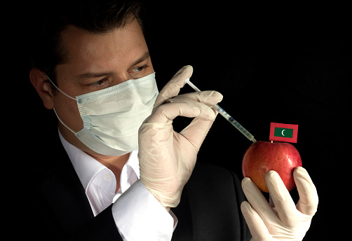Young businessman injecting chemicals into an apple with Maldivian flag on black background