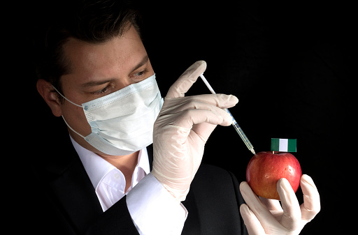 Young businessman injecting chemicals into an apple with Nigerian flag on black background