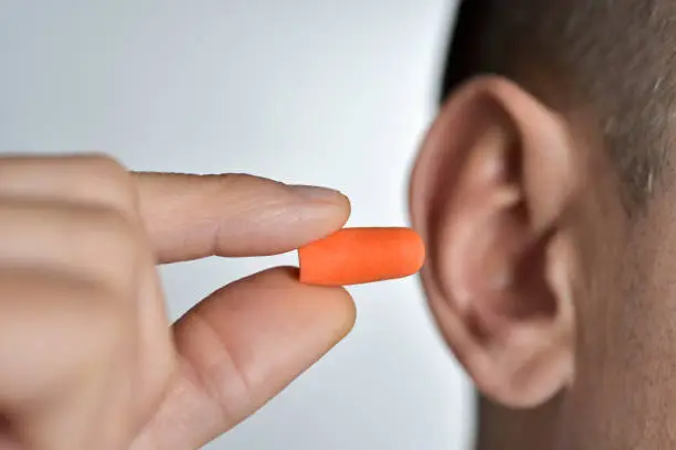 closeup of a young caucasian man inserting an orange earplug in his ear