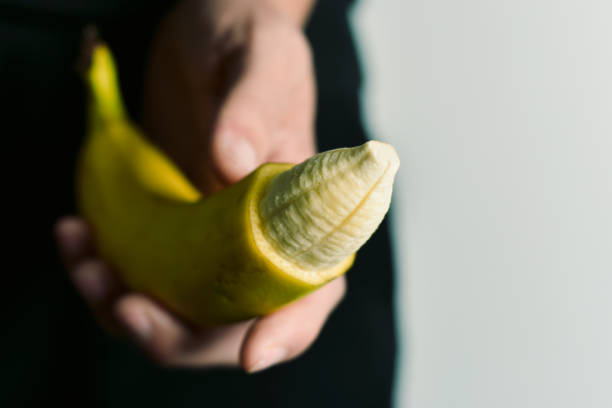 man with banana with its tip removed closeup of the hand of a young man with a banana with the tip of its skin removed, depicting a circumcised male member erection stock pictures, royalty-free photos & images