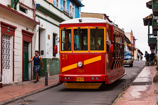 Bogotá, Colombia - July 20, 2016: A Tourist Bus modelled on the old trams that used to operate in the City over 50 years ago, drives down a street in the historical La Candelaria district of Bogotá, the Andean capital city of the South American country of Colombia. It is in this area that the Spanish Conquistador, Gonzalo Jiménez de Quesada founded the city in 1538. Many of the walls in this area are painted in the vibrant colours of Latin America. The sky is overcast: it will probably rain shortly. Photo shot on a cloudy morning; horizontal format. Copy space.