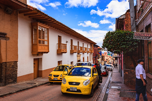 Bogotá, Colombia - July 20, 2016: Traffic seen driving uphill through the narrow streets of the historical La Candelaria district of Bogotá, the Andean capital city of the South American country of Colombia. It is in this area that the Spanish Conquistador, Gonzalo Jiménez de Quesada founded the city in 1538. Many of the walls in this area are painted with street art, legends of the pre Colombian era, or just in the vibrant colours of Latin America. The sky is overcast: it will probably rain shortly. Photo shot on a cloudy morning; horizontal format. Copy space.