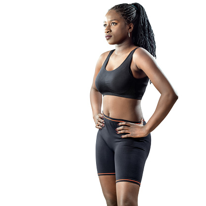 Medium shot of attractive african teen girl in sportswear standing with hands on hips. Young woman looking aside isolated on white background.