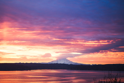 A beautiful morning view of the sunrise coming up behind Mt. Rainier, the pink, purple, and orange light casting it's colors onto the water of the Puget Sound.  As viewed from the Key Peninsula.