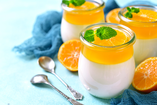 Panna cotta with orange jelly in a vintage jar on a light blue slate,stone or concrete background,traditional italian dessert.