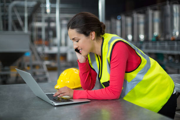 istock Female factory worker using laptop while talking on mobile phone 647089896