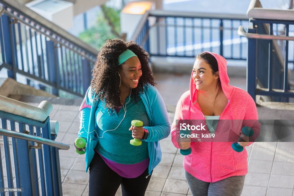 Two young women exercising, powerwalking up stairs Two multi-ethnic young women exercising together. They are looking at each other, smiling, as they climb a staircase holding hand weights. Exercising Stock Photo