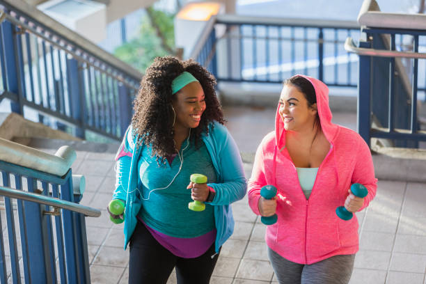 Two young women exercising, powerwalking up stairs Two multi-ethnic young women exercising together. They are looking at each other, smiling, as they climb a staircase holding hand weights. fitness tracker photos stock pictures, royalty-free photos & images