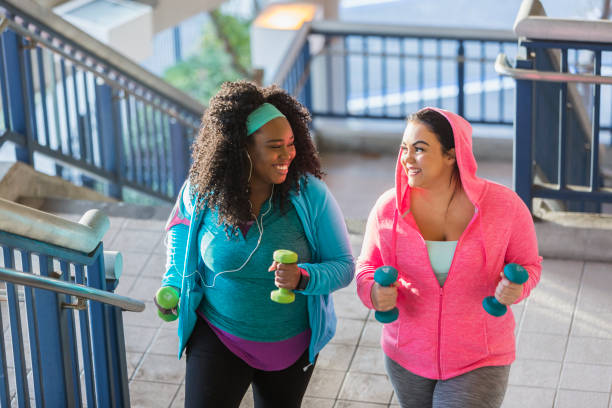 Two young women exercising, powerwalking up stairs Two multi-ethnic young women exercising together. They are looking at each other, smiling, as they climb a staircase holding hand weights. stout stock pictures, royalty-free photos & images