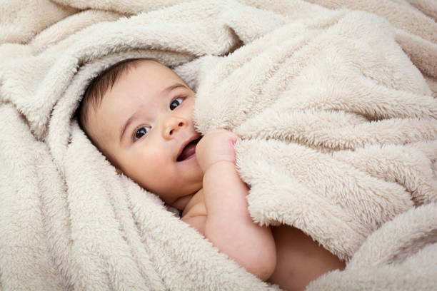 Cute baby boy in bed under a fluffy blanket stock photo