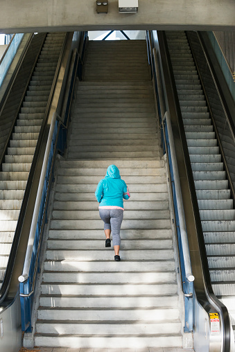 Rear view of a woman running up a steep flight of stairs. She is near the bottom and has a long way to go before she reaches the top.