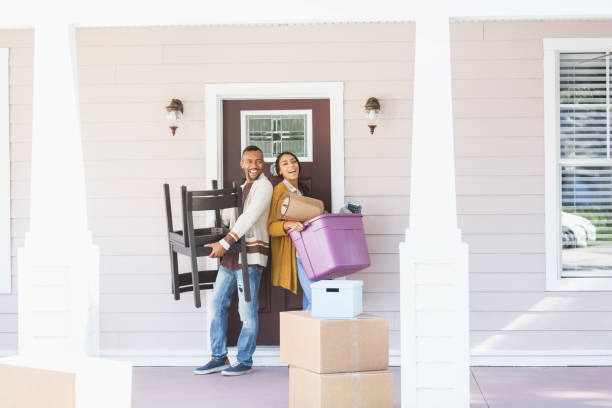 Young couple moving, carrying belongings thru front door