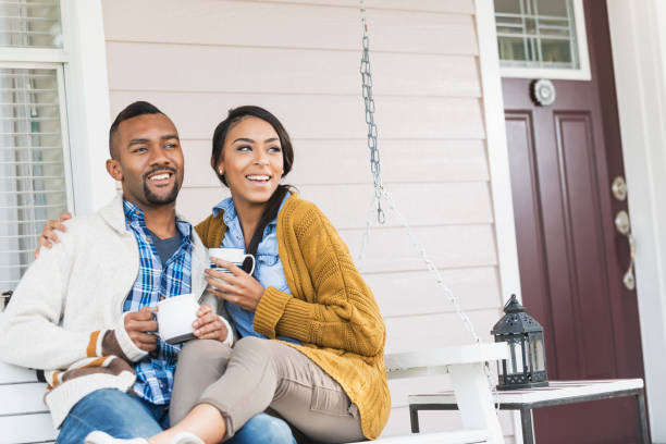 jóvenes mixtos par raza beber café en la oscilación de porche - couple outdoors coffee friendship fotografías e imágenes de stock