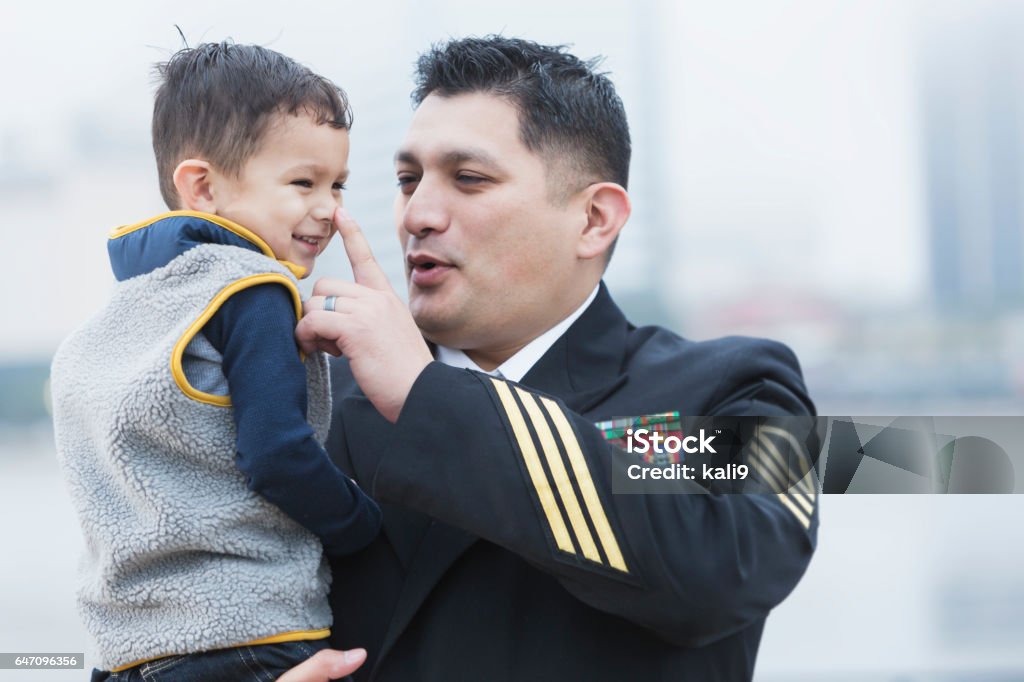 Hispanic military man holding 2 year old son An Hispanic man wearing a military uniform, holding his 2 year old son. The little boy is smiling as dad touches him affectionately on the tip of his nose. Navy Stock Photo