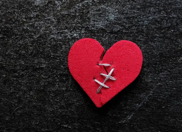 Red broken heart with thread stitches on dark background
