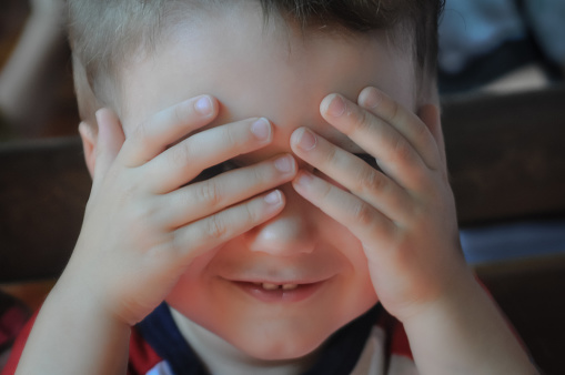 Close up of toddler boy playing peek-a-boo.
