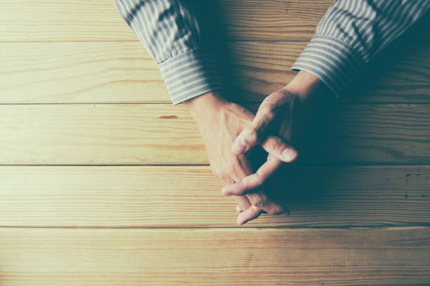 istock Close up on male hands folded in prayer at a wooden table 647129590