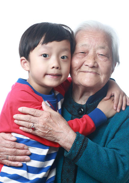 Happy Asian grandson and grandparents relax sitting on couch in the living room looking at camera. Family generation love bonding, people smiling and laughing together at home