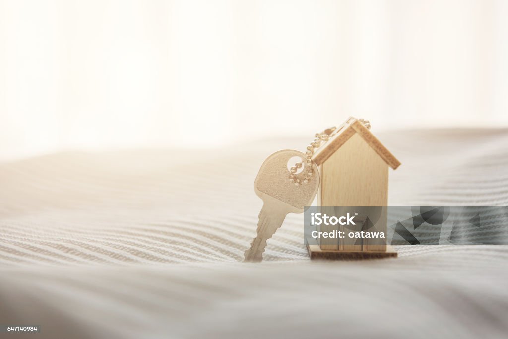 Symbol house with wood key on bed and sunlight. Symbol house with wood key on bed and sunlight, buy or rent estate concept, copy space. Moving House Stock Photo