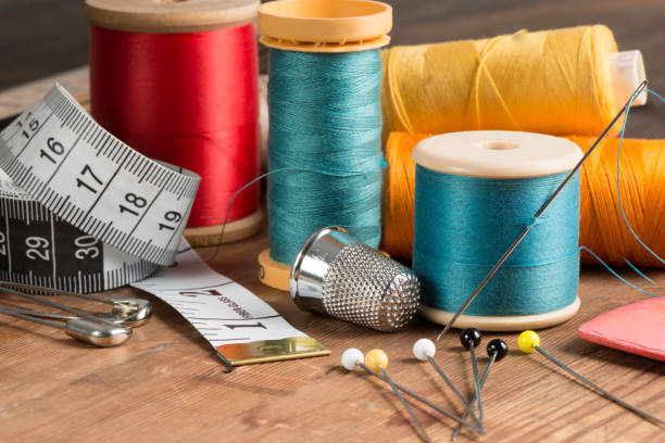 Basic Sewing Tools and Spools of Thread Basic sewing tools including needle, pins, thimble, tape measure, and tailor's chalk plus spools of thread on a wooden tabletop handspring stock pictures, royalty-free photos & images