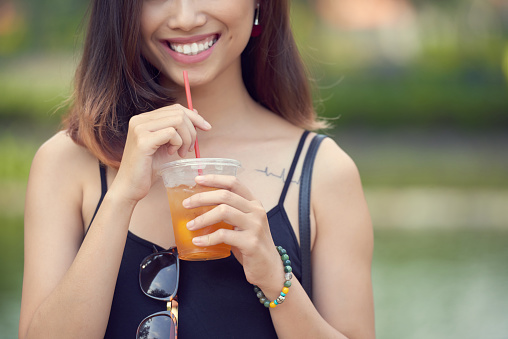 Cropped image of young woman enjoying glass of iced tea