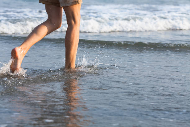 istock Closeup of a women's bare feet walking at a beach with a wave's edge foaming gently beneath them. 647188706