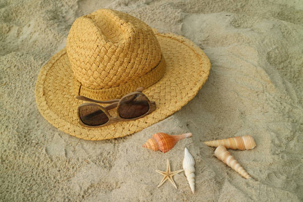 chapeau de paille brun clair et bruns lunettes de soleil sur la plage de sable avec petits coquillages - sandy brown photos photos et images de collection