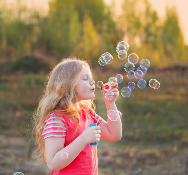 istock girl blowing soap bubbles outdoor at sunset 647191376