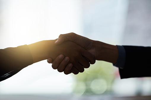 Cropped shot of two silhouetted businesspeople shaking hands in the office