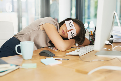 Shot of a tired businesswoman napping at her desk with adhesive notes on her eyes