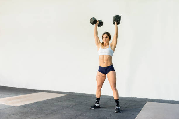 Horizontal rear view color image of muscled woman training at gym with dumbbells.