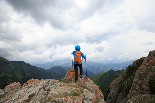 successful woman backpacker hiking on mountain peak cliff