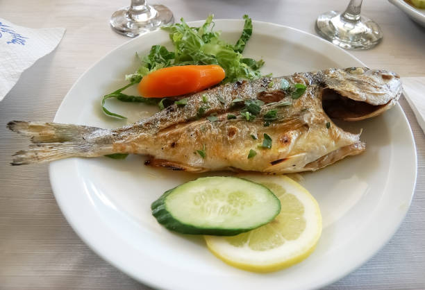 Roasted sea fish on a white plate in greek restaurant on coast peninsula Halkidiki.