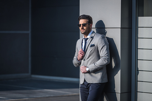 Fashionable businessman leaning on the wall of an office building and looking away