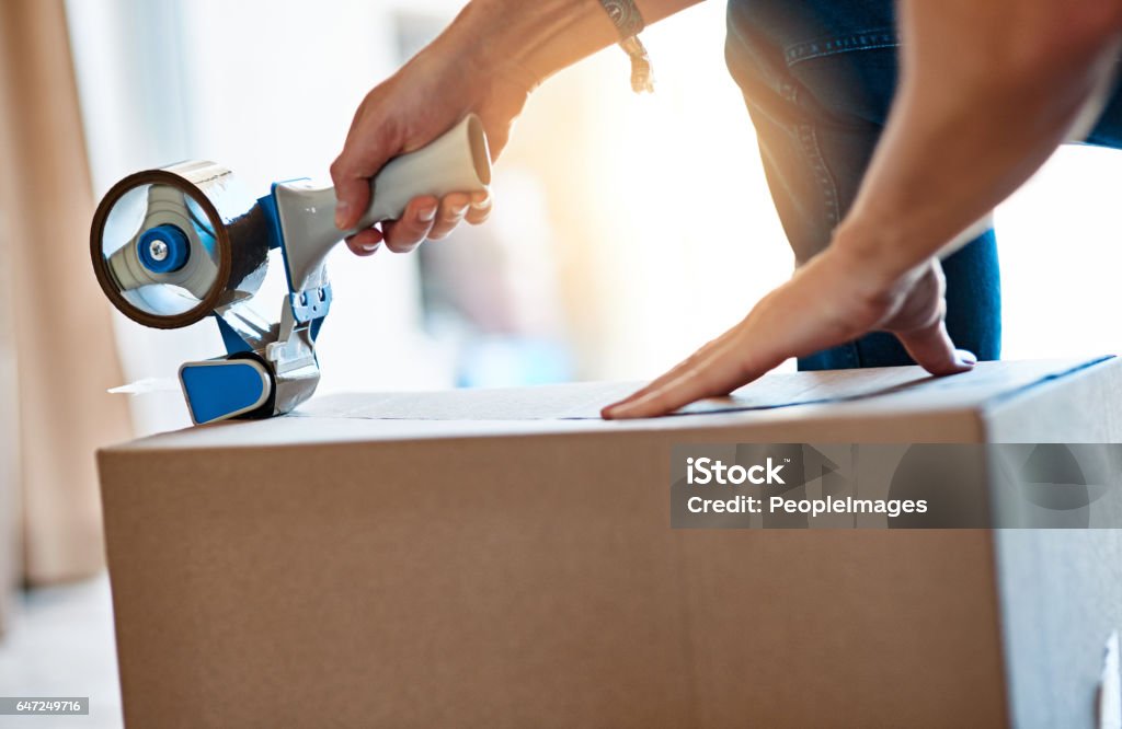 Wrap it, pack it, tape it Shot of an unrecognizable young man closing a cardboard box with tape at home Filming Stock Photo