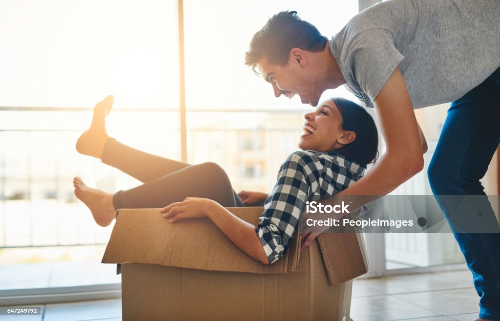 Filling our new home with fun Shot of a young man pushing his girlfriend around in a box while they move into their new home together Relocation Stock Photo