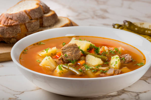 Bowl of vegetable beef soup with bread and hot chilli peppers in background stock photo