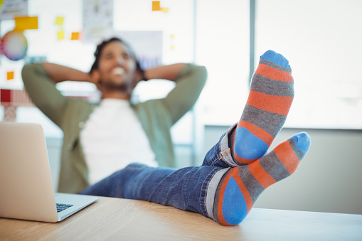 Male graphic designer relaxing with feet up at desk in office