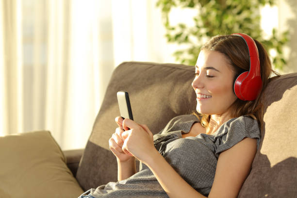 Teen listening music on line with a smart phone Single teen listening music on line with a smart phone and headphones sitting on a sofa n the living room at home free girl download stock pictures, royalty-free photos & images