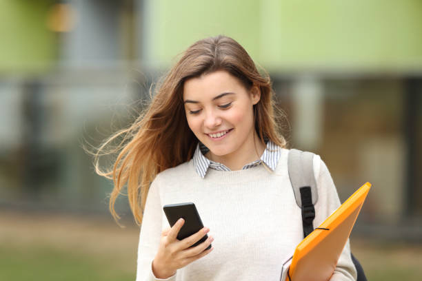 Student walking and reading phone messages Single student walking and reading mobile phone messages with a university building in the background education student mobile phone university stock pictures, royalty-free photos & images