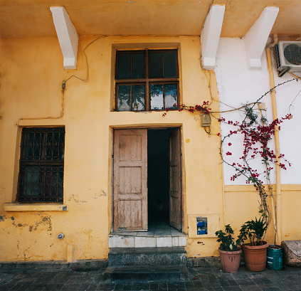 Mediterranean style white house exterior with blue door and window, flowering tree and romantic seating area. Traditional patio of Santorini.