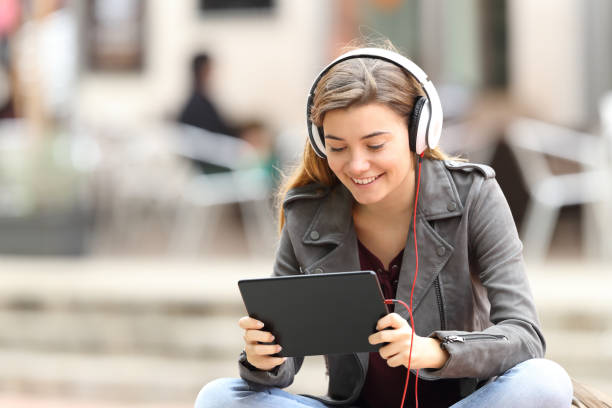 Girl learning on line with a tablet and headphones Beautiful fashion girl learning on line with a tablet and headphones sitting on a bench in the street entertainment equipment stock pictures, royalty-free photos & images
