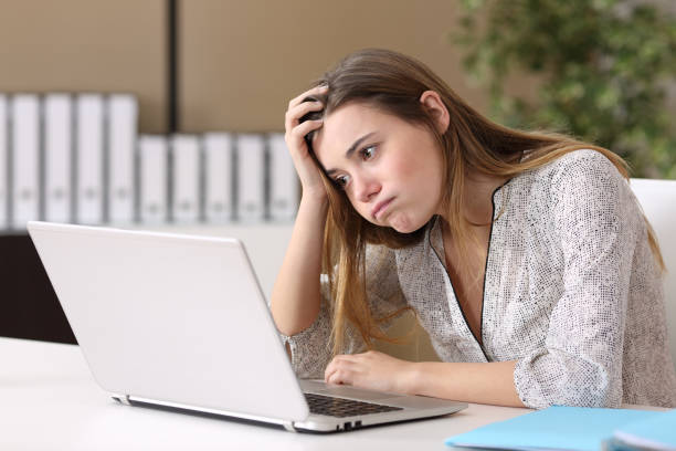 Frustrated intern working on line at office Frustrated intern trying to work on line with a laptop in a difficult assignment in a desktop with an office background career girl stock pictures, royalty-free photos & images