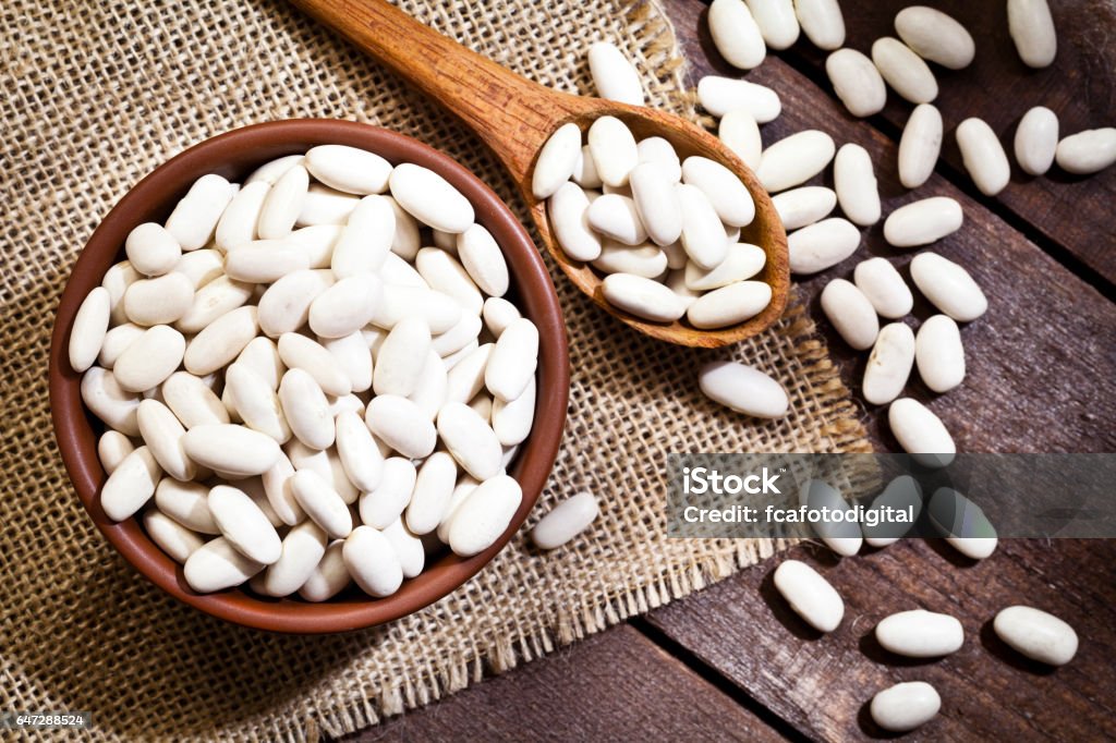 Black white in a bowl Top view of a brown bowl filled with white beans shot on rustic wood table. A wooden spoon is beside the bowl with some beans on it. DSRL studio photo taken with Canon EOS 5D Mk II and Canon EF 100mm f/2.8L Macro IS USM Bean Stock Photo