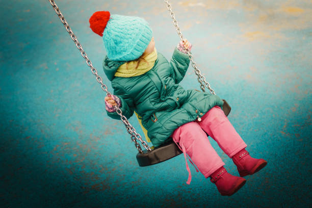 mała dziewczynka kołysząca się na huśtawce - winter child coat baby girls zdjęcia i obrazy z banku zdjęć
