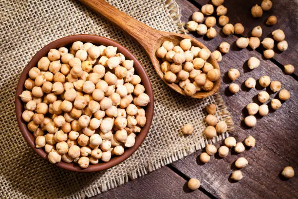 Top view of a brown bowl filled with chickpeas shot on rustic wood table. A wooden spoon is beside the bowl with some lentils on it. DSRL studio photo taken with Canon EOS 5D Mk II and Canon EF 100mm f/2.8L Macro IS USM