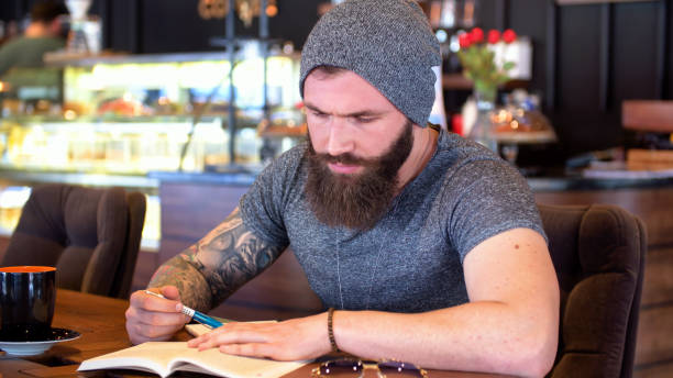 istock Bearded and tattooed hipster reading a book the cafe 647310408