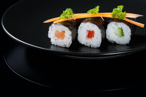 istock Fresh rolls on a plate, roll with salmon, cucumber and pepper served with carrot slices and parsley, black background 647319748